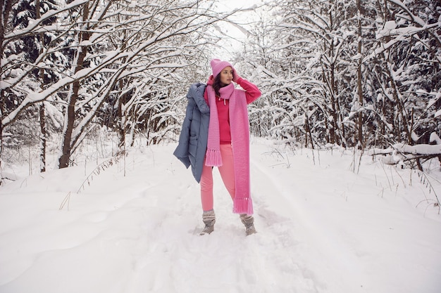 Woman enjoy in pink clothes a jacket a knitted scarf and a hat stands in a snowy forest in winter