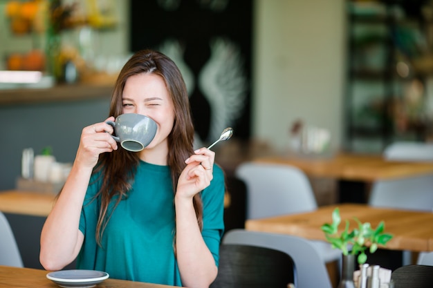 Woman enjoy tasty coffee having breakfast at outdoor cafe. Happy young urban woman drinking coffee