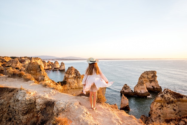 Woman enjoying great view on the rocky coastline during the sunrise in Lagos on the south of Portugal