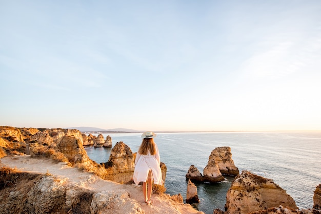 Woman enjoying great view on the rocky coastline during the sunrise in Lagos on the south of Portugal