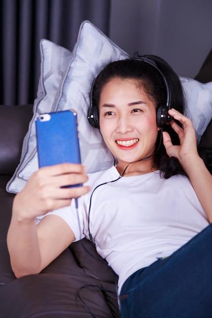 woman enjoying music in headphones, making selfie with cellphone while lying on sofa