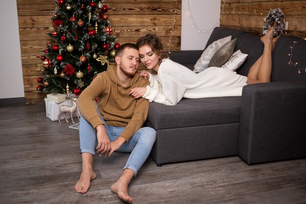 Woman enjoying time together with her boyfriend at home. Christmas tree on background.