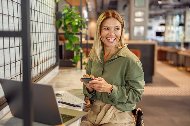 Photo woman entrepreneur is using phone in coworking during work on laptop distance work concept