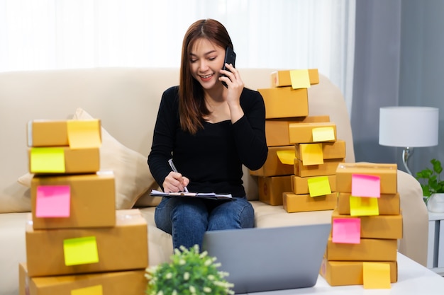 Woman entrepreneur talking with customer on a mobile phone and writing product order at home office