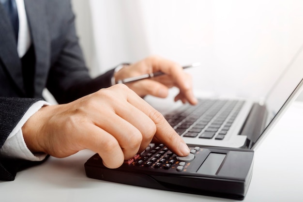 Woman entrepreneur using a calculator with a pen in her hand calculating financial expense at home office