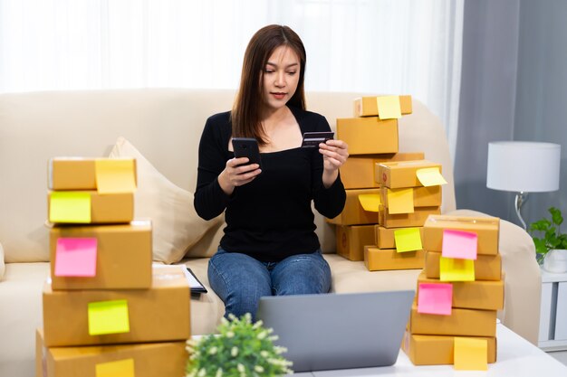 Woman entrepreneur using a smartphone with credit card at home office