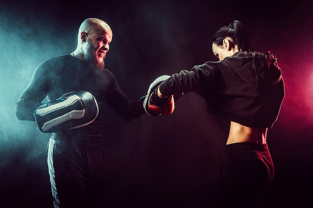 Woman exercising with trainer at boxing and self defense lesson, studio, smoke on space