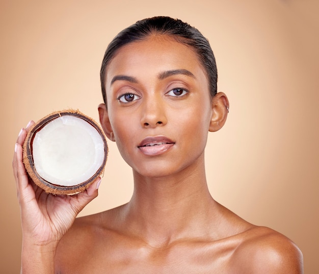 Woman face coconut fruit and beauty healthy skincare or vegan cream on brown studio background Portrait of Indian person in natural product for dermatology eco friendly cosmetics and oil benefits