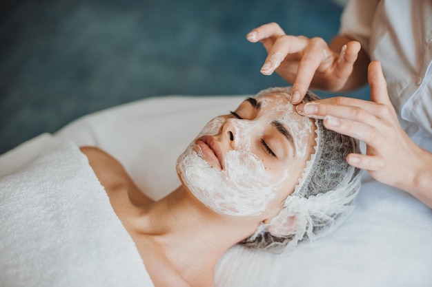 Woman face getting facial care with cream by beautician hands at spa salon closeup portrait