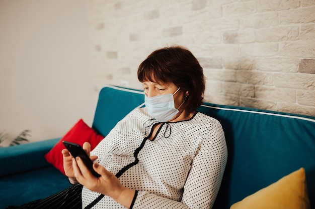 woman in face mask sitting at home on the sofa and calling doctor