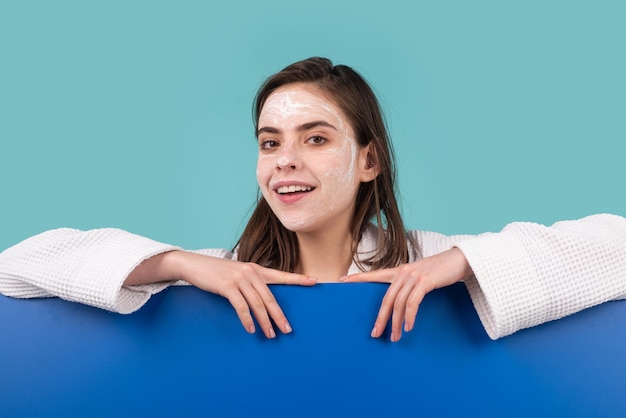 Woman facial mask, face clay. Beautiful woman with cosmetic facial procedure, spa skin concept. Spa girl with copy space for text. Proposing a product. Gestures for advertisement. Blue background.