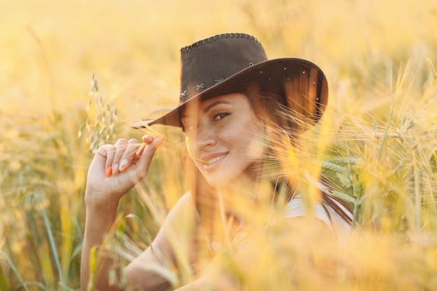 Woman farmer in cowboy hat at agricultural field on sunset