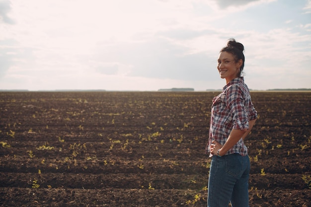 Woman farmer standing and looking agricultural field soil