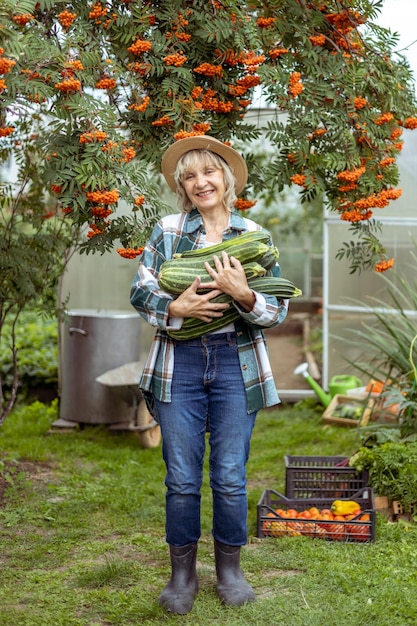 A woman farmer stands in the middle of a vegetable garden holding a crop of zucchini in her hands