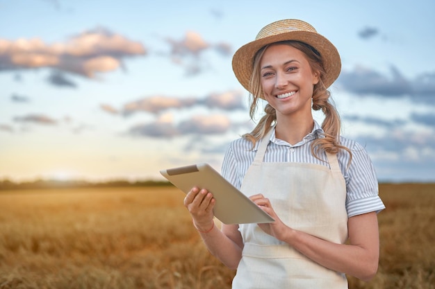 Woman farmer straw hat smart farming standing farmland smiling using digital tablet Female agronomist specialist research monitoring analysis data agribusiness