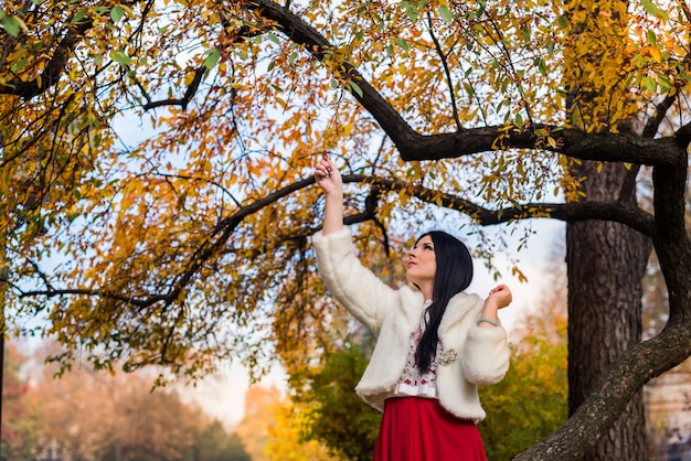 Woman in fashion dress and fur coat posing in autumn park