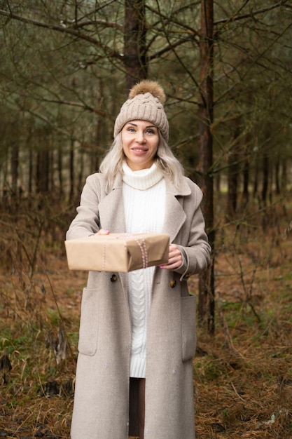 Woman in fashion warm clothes holding gift box in Kraft paper packaging on nature background