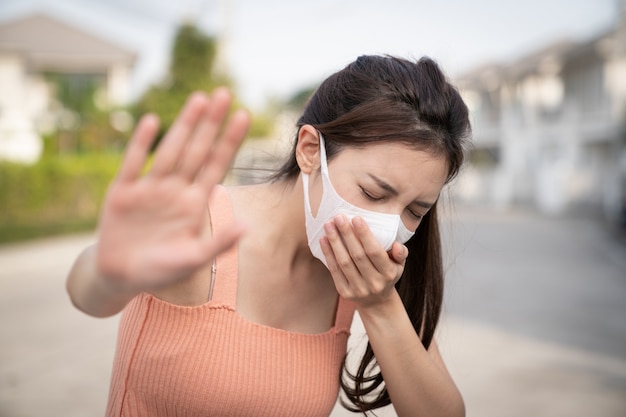 Woman feeling sick, coughing or sneezing. holds the hand in front of her, sign to stop. She wearing protective mask.