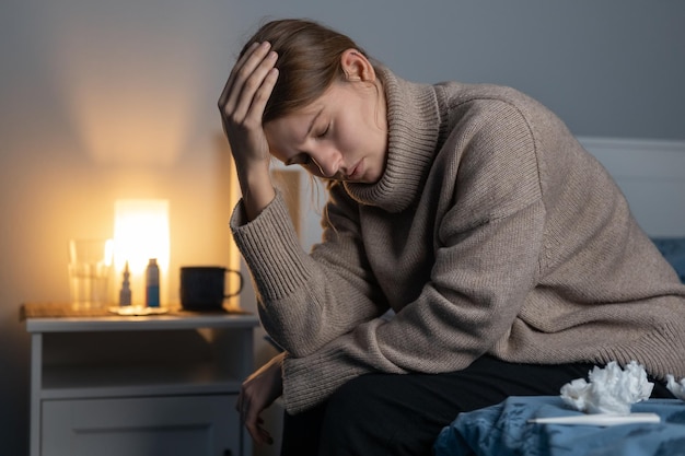 Woman feeling sick sitting on bed and holding her head Female suffering from headache or migraine