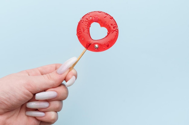 Woman female hand holding heart shaped lollipop on blue background