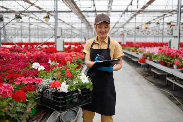 Woman fills out inspection document in a greenhouse with flowers