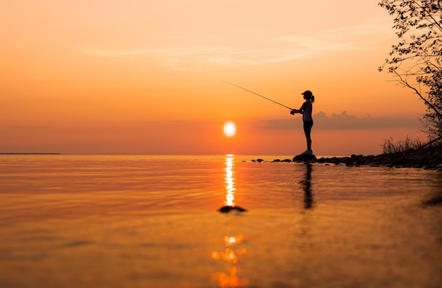 Woman fishing on Fishing rod spinning at sunset background.