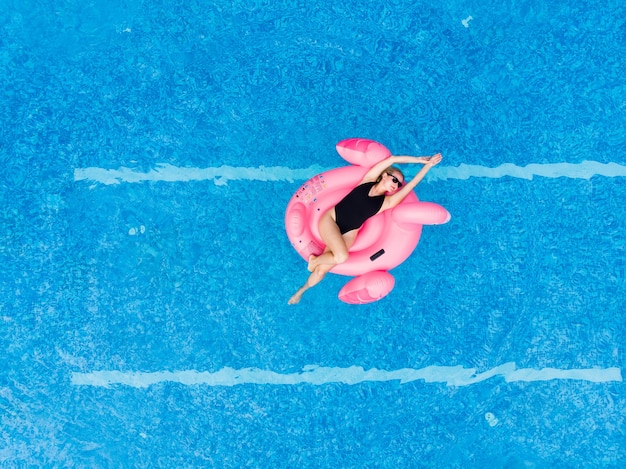 Woman on flamingo pool float in pool, drone aerial view