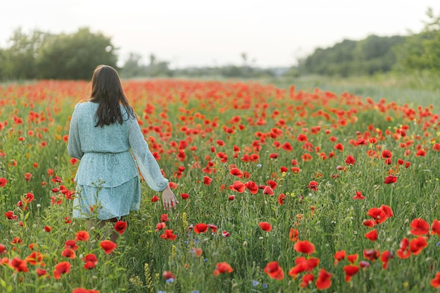 Woman in floral dress walking in poppy field in evening summer countryside Atmospheric moment Young female relaxing and gathering wildflowers in meadow Rural simple life