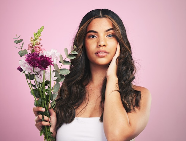 Woman flowers and portrait in studio for skincare cosmetics and natural aesthetic on pink background Face model and eco beauty with floral plants sustainability and bouquet for vegan dermatology