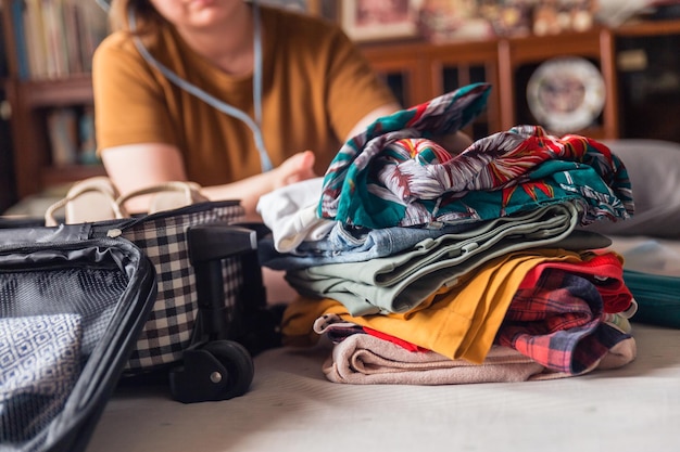 A woman folds clothes from a pile of selected belongings and puts them in luggage on the bed Packing to go on a getaway vacation Focus on clothes