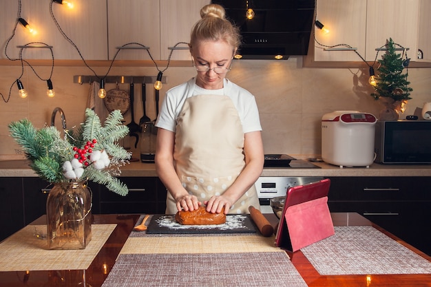 Woman following recipe on digital tablet and kneads the dough for cooking christmas gingerbread cookies on her kitchen.