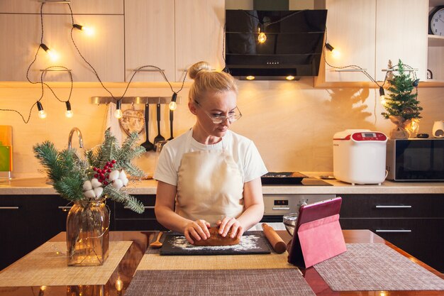 Woman following recipe on digital tablet and kneads the dough for cooking christmas gingerbread cookies on her kitchen.