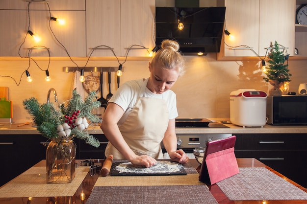 Woman following recipe on digital tablet and kneads the dough for cooking christmas gingerbread cookies on her kitchen.