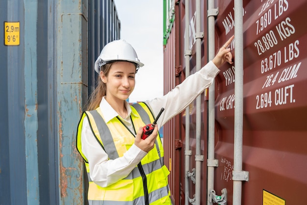 Woman foreman smile using walkie talkie in front of Cargo forklift in warehouse Manager in white helmet Safety Supervisor in Container Custom Terminal port concept import export