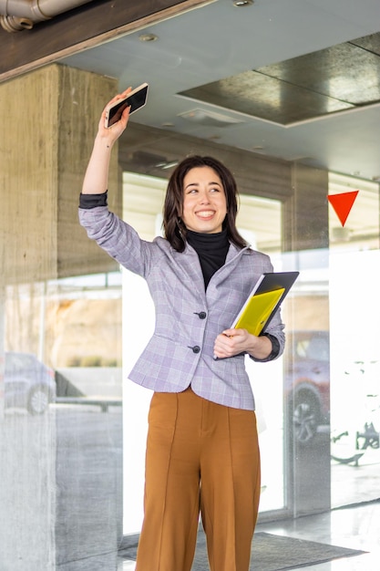 Woman in formal suit saying goodbye to a person outdoors Portrait of smiling business girl waving goodbye to a person in the distance