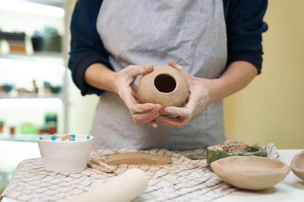 Woman forming clay pot shape by hands closeup in artistic studio