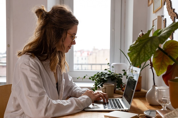 Woman freelancer/designer working on computer from home office. Cozy workplace surrounded by plants. Remote work