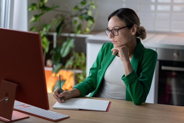 Woman freelancer makes plan for business project working at computer in cozy home office with plant