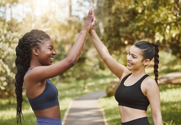 Woman friends and high five in nature for fitness teamwork or outdoor training goals together Female person touching hands in celebration for team exercise running or sports practice at the park