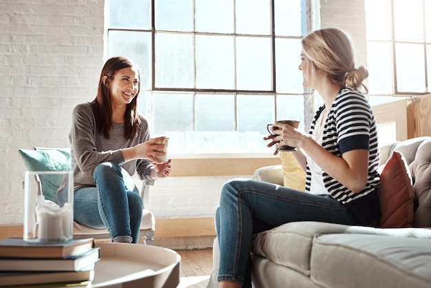 Woman friends and smile for coffee conversation or social catch up relaxing together on living room sofa at home Happy women enjoying tea time chatting or gossip with drink in apartment on couch