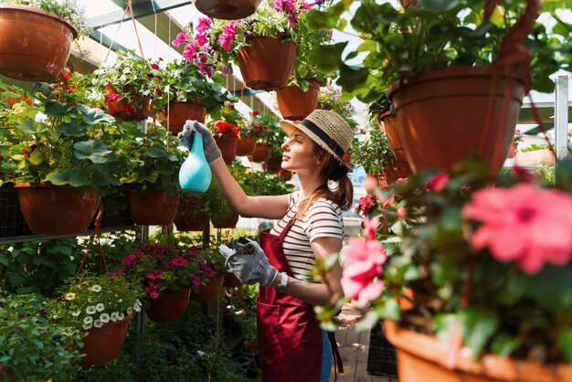 Woman gardener in hat and gloves works with flowers in the greenhouse