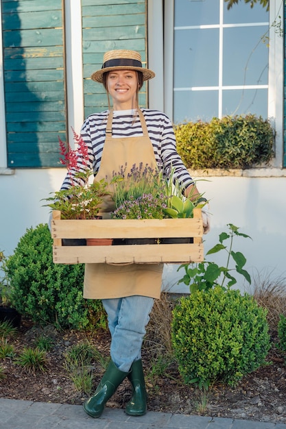 Woman gardener holding a wooden box full of plants in garden