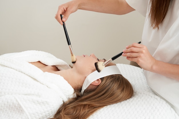 Woman gets brushes treatment at beauty clinic face skin care concept relaxing in spa salon