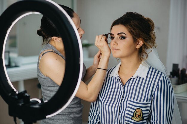 A woman gets her make up done in front of a mirror