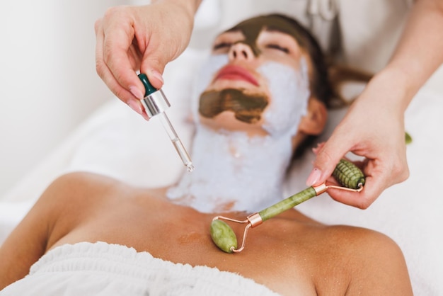 Woman getting a gua sha treatment with a jade roller on decollete zone at the beauty salon.