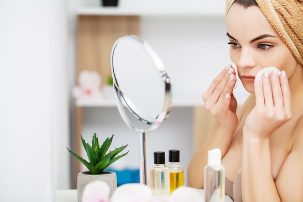 Woman getting ready for work doing morning makeup in bathroom mirror at home