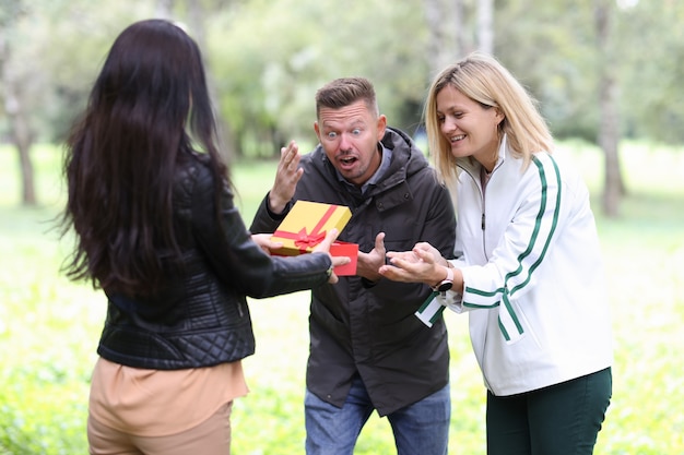 Woman giving gift in red box young couple in park choosing gift for family celebrations concept