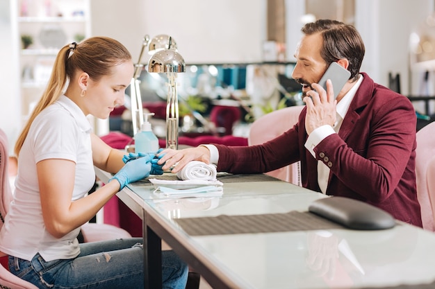 Woman giving manicure and vigorous mature man gossiping on phone