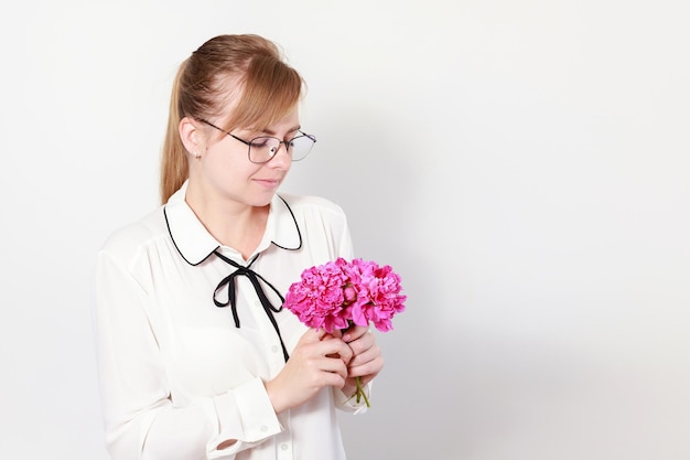 A woman in glasses and a blouse with peonies on a light background