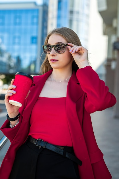 Woman in glasses and classic brand clothes holding a cup of coffee and smiling on City